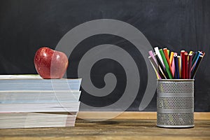 Red apple, books and penciles on wooden table and blackdoard background.school for kids