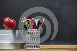 Red apple, books and penciles on wooden table and blackdoard background.school for kids