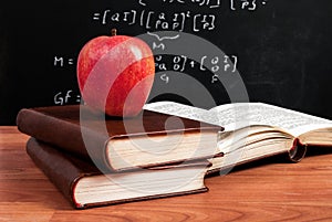 Red apple on books and school blackboard with mathematical equations in the classroom
