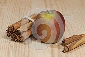 Red apple with a cinnamon stick; photo on wooden background