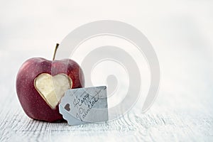 Red apple with cut out heart on lichtgrey wooden underground