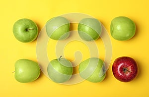 Red apple among green ones on color background, top view.