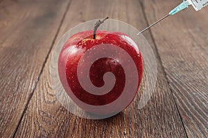 Red apple injecting a needle or syringe and chemical pesticides on a wooden background. Specific pesticide residues in apples,