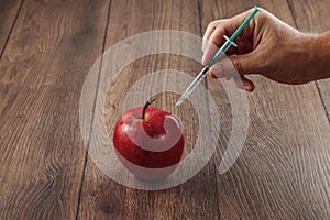 Red apple injecting a needle or syringe and chemical pesticides on a wooden background. Specific pesticide residues in apples,