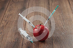 Red apple injecting a needle or syringe and chemical pesticides on a wooden background. Specific pesticide residues in apples,