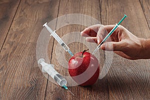 Red apple injecting a needle or syringe and chemical pesticides on a wooden background. Specific pesticide residues in apples,