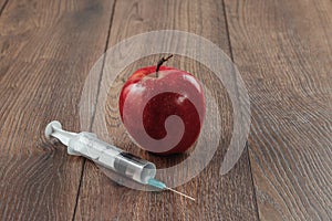 Red apple injecting a needle or syringe and chemical pesticides on a wooden background. Specific pesticide residues in apples,