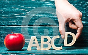 Red apple and letters of the ABCD. The hand puts the letter D to the others in a row. Apple for the teacher. Concept of education,