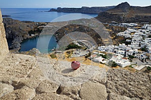 A red apple lies on the fortress wall in the ancient Acropolis of Lindos in August and a picturesque view of St. Paul\'s Bay.