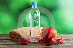 Red apple with measuring tape and bottle of water on grey wooden background.