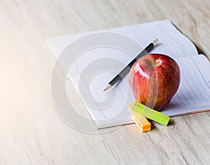 Red apple, pen And a white note book with a wooden background,selective Focus