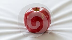 Red apple with a shiny smooth surface sits on a white slightly
