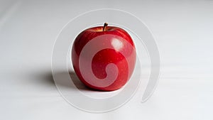 Red apple with a smooth, shiny surface sits on a plain, white background. The apple is round and