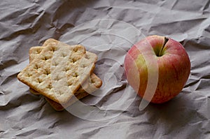 Red apple and square crackers lying on crumpled wrapping paper