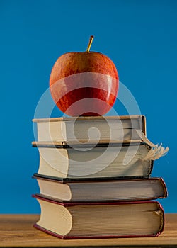 Red apple on a stack of books lying on the surface of an oak table