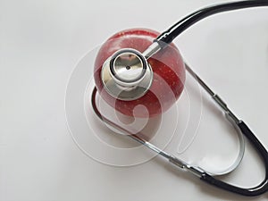 Red apple, with a stethoscope, on a white background, top view, focus on the foreground.