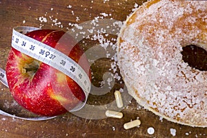 Red apple and tape measure as concept of healthy food and doughnut surrounded with pills as unhealthy food.