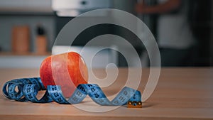 Red apple and tape measure on kitchen table unrecognizable blurred African man athlete opening fridge searching