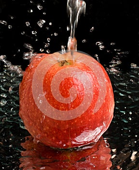 Red apple under water stream with splashes