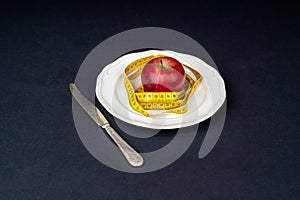 Red apple in a white plate wrapped with a tape measure