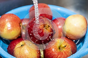 Red apples in a bowl under running water while washing the fruit