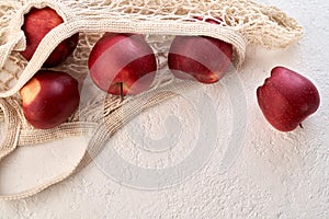 Red apples in an ecological reusable mesh bags made of organic cotton on a white background with copy space