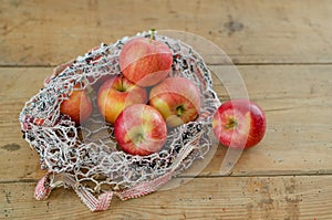 Red apples are in fishnet on wooden table