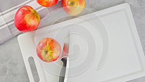 Red apples and a knife close-up on a white cutting board, flat lay