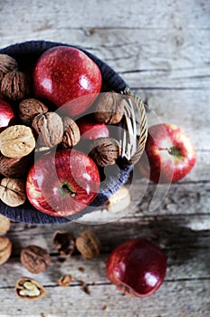 Red apples and walnuts in shells filled in basket, autumn scene