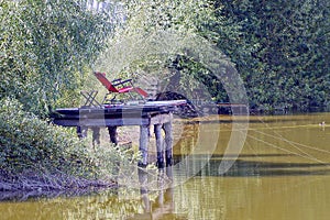 Red armchair on a wooden bridge with fishing rods over the water