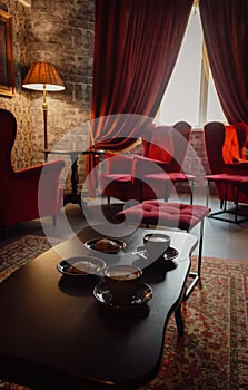 Red armchairs with coffee cups on table in cozy classic interior. Antique living room with red curtains and armchairs.