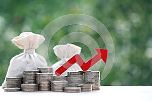 Red arrow graph on stack of coins money and money bag on natural green background, Business investment and Risk management concept