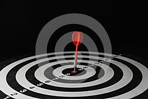 Red arrow hitting target on dart board against black