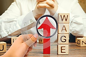 Red arrow up near wooden blocks with the word Wage and a businessman. Salary increase concept. Wages rate. Revenue growth and