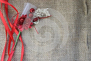 Red artificial flower with red festive ribbons on a background of brown old linen fabric texture, linen natural material with a co