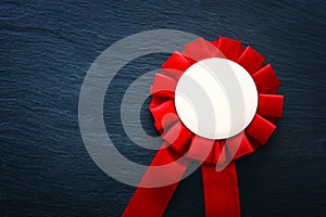 Red award rosette with ribbons over black textured background, ready for mock up