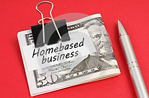 On a red background lies a pen and dollars clamped with a clip with the inscription on paper - Homebased business