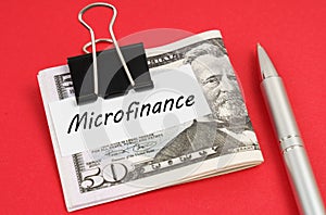 On a red background lies a pen and dollars clamped with a clip with the inscription on paper - Microfinance photo