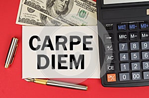 On a red background, among the money, a calculator and a pen lies a sign with the text - CARPE DIEM
