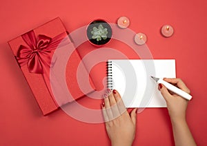 On a red background is a red gift box. Writing ideas and goals in a notebook.