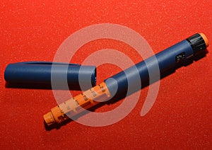 On a red background, a syringe pen for the introduction of insulin to a patient with diabetes, endocrinological diseases