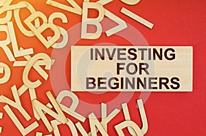 On a red background, there are wooden letters and a plate with the inscription - INVESTING FOR BEGINNERS