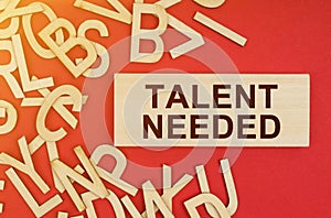 On a red background, there are wooden letters and a plate with the inscription -Talent Needed