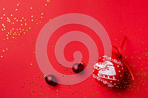 Red ball with pattern for the Christmas tree with golden confetti and toys on a red background. Top view, minimal christmas style