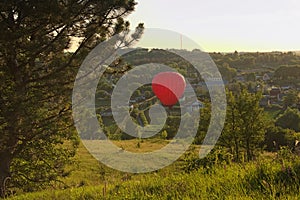 Red balloon flies over a village located between picturesque hills. Clear blue sky without clouds, during sunset