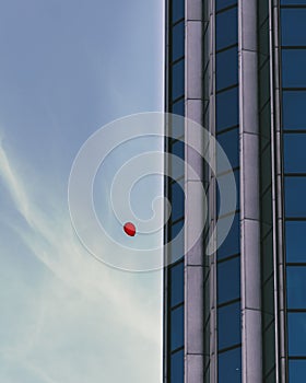 Red balloon flying near the exterior of abuilding with glass windows