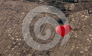 Red balloon in the shape of red heart hovers over field as a background