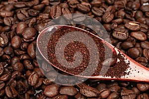 Red bamboo spoon with ground coffee, lies on roasted coffee beans, close-up, isolated on a white background