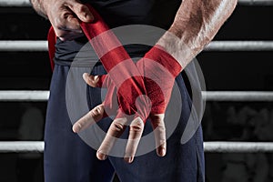 Red bandages on the hands of a kickboxer against the background of the ropes of the ring. The concept of mixed martial arts