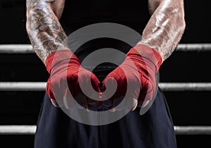 Red bandages on the hands of a kickboxer against the background of the ropes of the ring. The concept of mixed martial arts